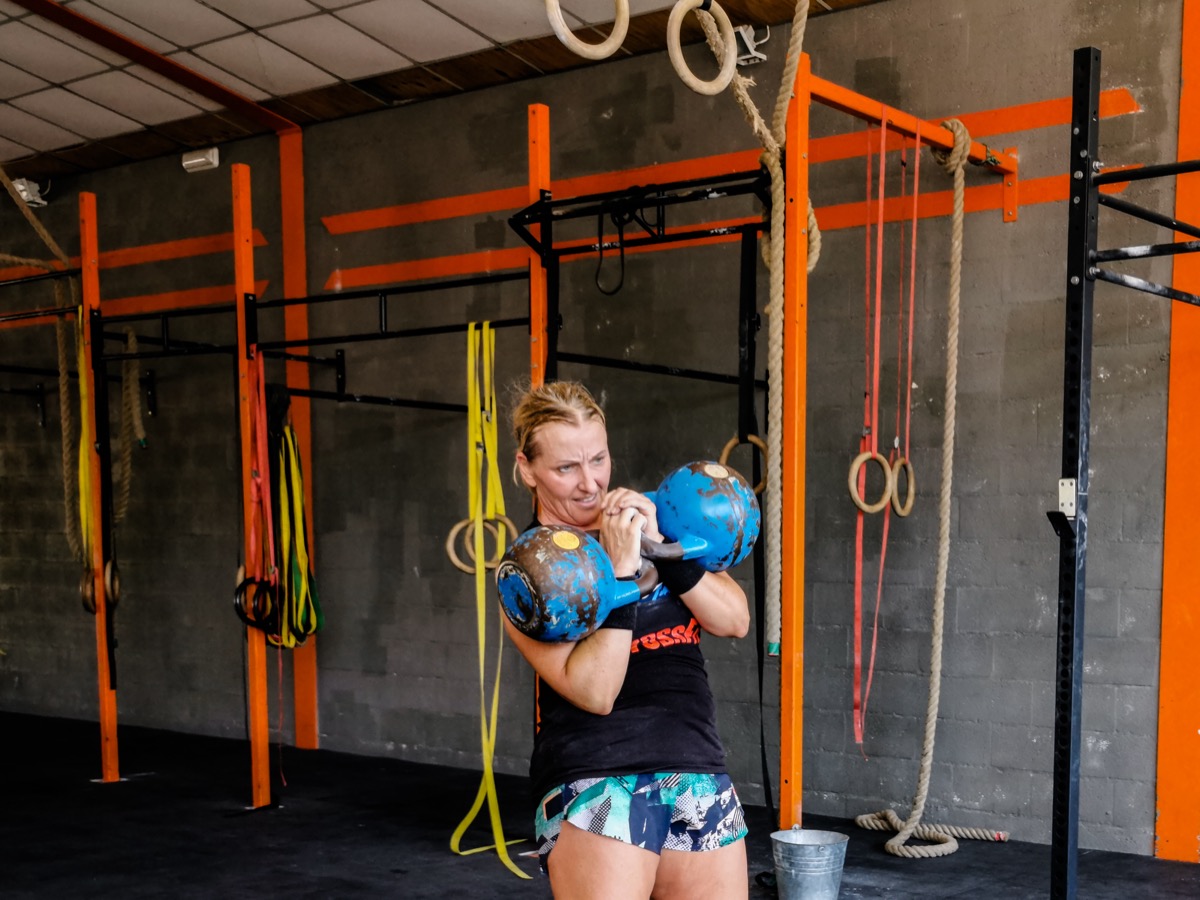 Anna holding two competition kettlebells in rack position in a CrossFit gym
